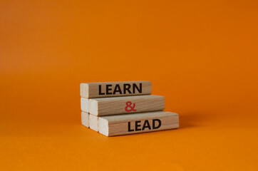 Learn and lead symbol. Concept words Learn and lead on wooden blocks. Beautiful orange background....
