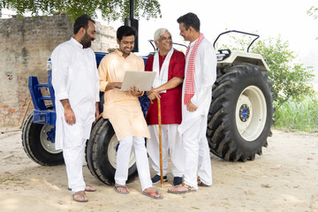 Young man guiding farmer about modern farming techniques using laptop on agriculture field.