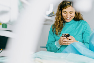 Smiling dentist in the operating room uses mobile phone