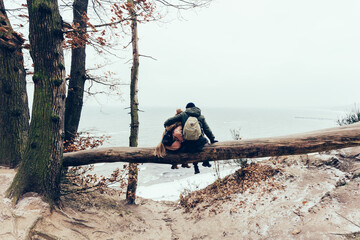 Couple trekking in winter sitting on tree by the sea