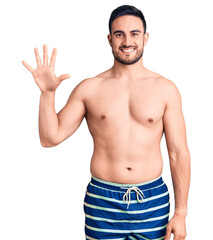 Young handsome man wearing swimwear showing and pointing up with fingers number five while smiling confident and happy.