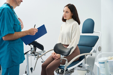 Woman sits on medical chair and listens to a doctor - obrazy, fototapety, plakaty