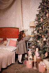 Vinnytsia, Ukraine. December 25, 2021: A girl with a bow on her head at home near the Christmas tree is looking for gifts from her parents for Christmas