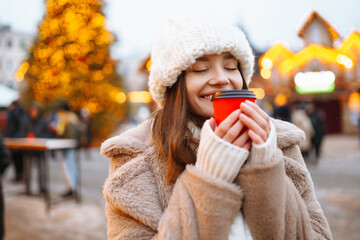 Young woman with coffee in winter over outdoor ice skating rink on background. Festive Christmas...