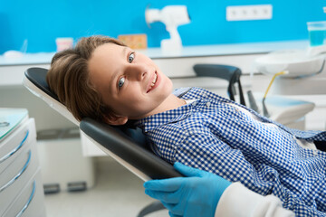 Smiling teenager sits in a dental chair among special equipment