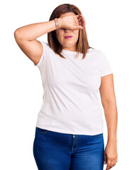 Middle age latin woman wearing casual white tshirt covering eyes with arm, looking serious and sad. sightless, hiding and rejection concept