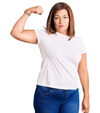 Middle age latin woman wearing casual white tshirt strong person showing arm muscle, confident and proud of power
