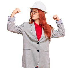 Young redhead woman wearing architect hardhat showing arms muscles smiling proud. fitness concept.