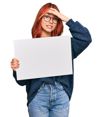 Young redhead woman holding blank empty banner stressed and frustrated with hand on head, surprised and angry face