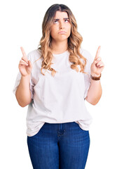 Young caucasian woman wearing casual clothes pointing up looking sad and upset, indicating direction with fingers, unhappy and depressed.