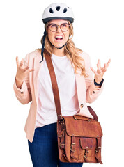 Young caucasian woman wearing bike helmet and leather bag crazy and mad shouting and yelling with aggressive expression and arms raised. frustration concept.