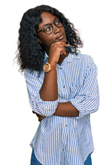 Fototapeta na wymiar Beautiful african young woman wearing casual clothes and glasses with hand on chin thinking about question, pensive expression. smiling with thoughtful face. doubt concept.