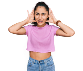 Hispanic teenager girl with dental braces wearing casual clothes trying to hear both hands on ear gesture, curious for gossip. hearing problem, deaf