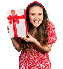 Young hispanic girl holding gift smiling and laughing hard out loud because funny crazy joke.