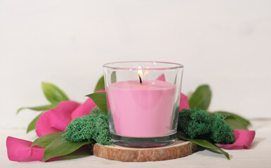 Obraz na płótnie Canvas floral fragranced burning candle with green leaves, moss and petals. home fragrances, cozy home ambience, romantic decor for valentines. 