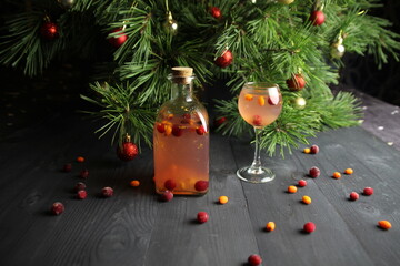 Winter drink in bottle and glass with buckthorn and cranberries and christmas pine tree decoration on table