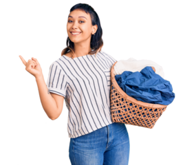 Young woman holding laundry basket smiling happy pointing with hand and finger to the side