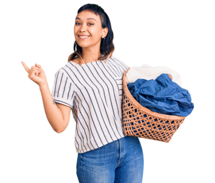 Young woman holding laundry basket smiling happy pointing with hand and finger to the side - Powered by Adobe