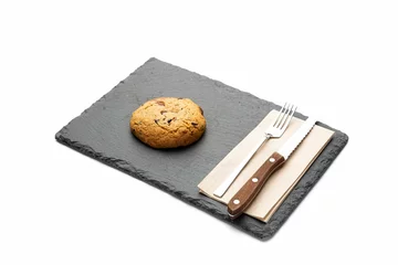  Closeup of a cookie on a black tray with silverware on the side isolated on a white background. © Galip Kürkcü/Wirestock Creators