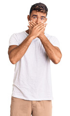 Young hispanic man wearing casual white tshirt shocked covering mouth with hands for mistake. secret concept.