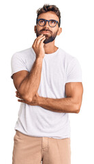 Young hispanic man wearing casual clothes and glasses with hand on chin thinking about question, pensive expression. smiling and thoughtful face. doubt concept.