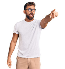 Young hispanic man wearing casual clothes and glasses pointing with finger surprised ahead, open...