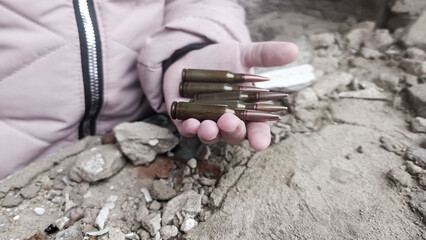 Fototapeta na wymiar Bullets in the hands of a child. Cartridges in children's hands. War in Ukraine. Russian aggression in Ukraine. Children against war. Peace concept. A child plays with cartridges in the ruins.
