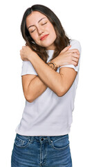 Young beautiful woman wearing casual white t shirt hugging oneself happy and positive, smiling confident. self love and self care