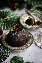 Fototapeta na wymiar Traditional Christmas pudding decorated with holly on vintage plate and handmade paper decorations on linen tablecloth.