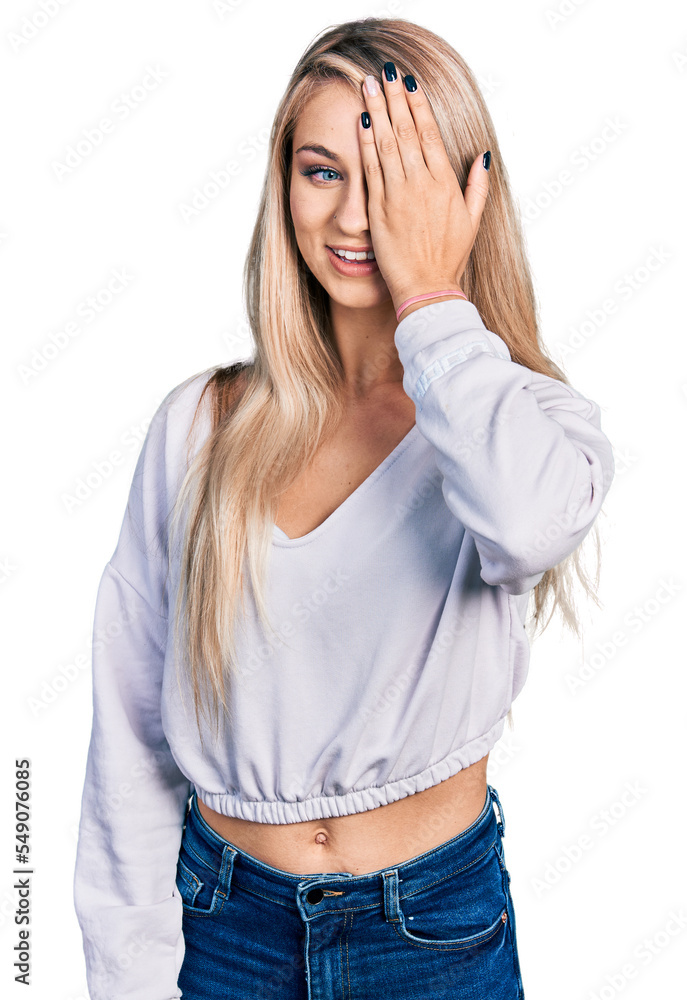 Sticker Beautiful young blonde woman wearing casual white sweater covering one eye with hand, confident smile on face and surprise emotion.