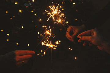 Happy New Year! Friends celebrating with burning sparklers in hands against christmas tree lights...