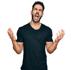 Hispanic man with beard wearing casual black t shirt crazy and mad shouting and yelling with...