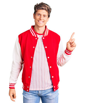 Young handsome man wearing baseball uniform with a big smile on face, pointing with hand finger to the side looking at the camera.