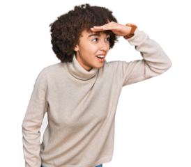 Young hispanic girl wearing wool winter sweater very happy and smiling looking far away with hand over head. searching concept.