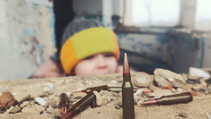 Child in fear during the war. War in Ukraine. Children against war. Bullets against the background of a frightened child. Bullet against the background of children's eyes. The child plays with bullets