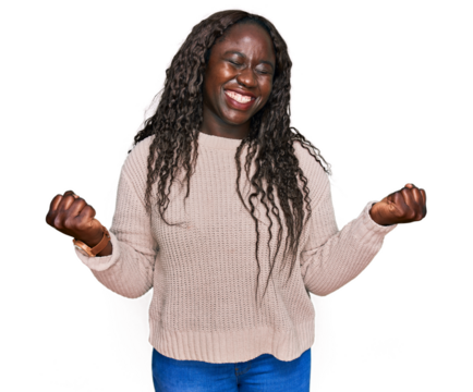 Young african woman wearing wool winter sweater very happy and excited doing winner gesture with arms raised, smiling and screaming for success. celebration concept.