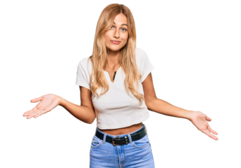 Beautiful blonde young woman wearing casual white tshirt clueless and confused expression with arms and hands raised. doubt concept.