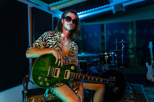 Extravagant man sitting on amplifier with guitar