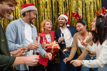 Excited multiethnic business people holding champagne and sparklers during Christmas party in office
