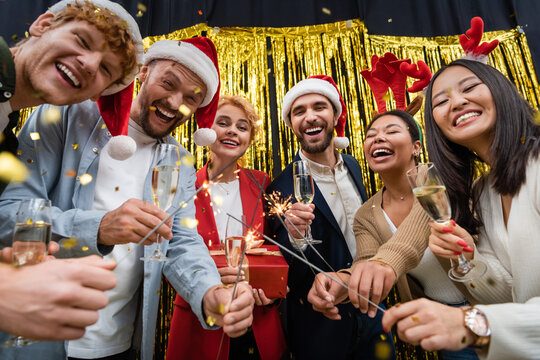 Low Angle View Of Multiethnic Business People Holding Sparklers And Champagne During New Year Party In Office