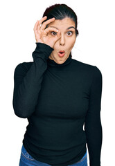 Young hispanic woman wearing casual clothes doing ok gesture shocked with surprised face, eye looking through fingers. unbelieving expression.