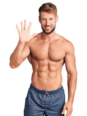 Young caucasian man standing shirtless showing and pointing up with fingers number five while smiling confident and happy.