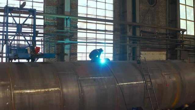 Welding large diameter pipes with pre-heated flexible ceramic heating elements in the field. A welder welds large pipes in a factory.