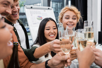 Multicultural business people clinking blurred glasses of champagne in office