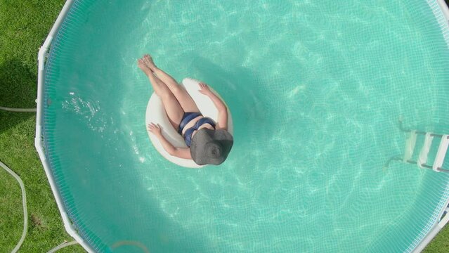 Aerial view of a woman in a hat swimming in a round pool