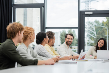 bearded man and asian woman smiling at interracial business colleagues in meeting room