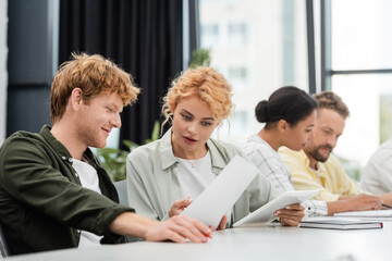 smiling businesswoman showing document to colleague near interracial team on blurred background