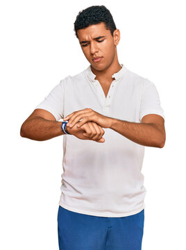 Young arab man wearing casual clothes checking the time on wrist watch, relaxed and confident