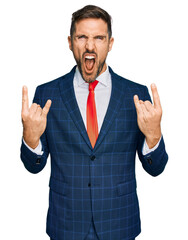 Handsome man with beard wearing business suit and tie shouting with crazy expression doing rock symbol with hands up. music star. heavy concept.