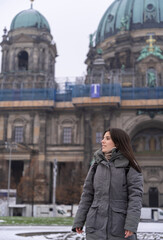 Fototapeta na wymiar Young female tourist walking in the park in front of the Berlin Cathedral with snow all over the ground.